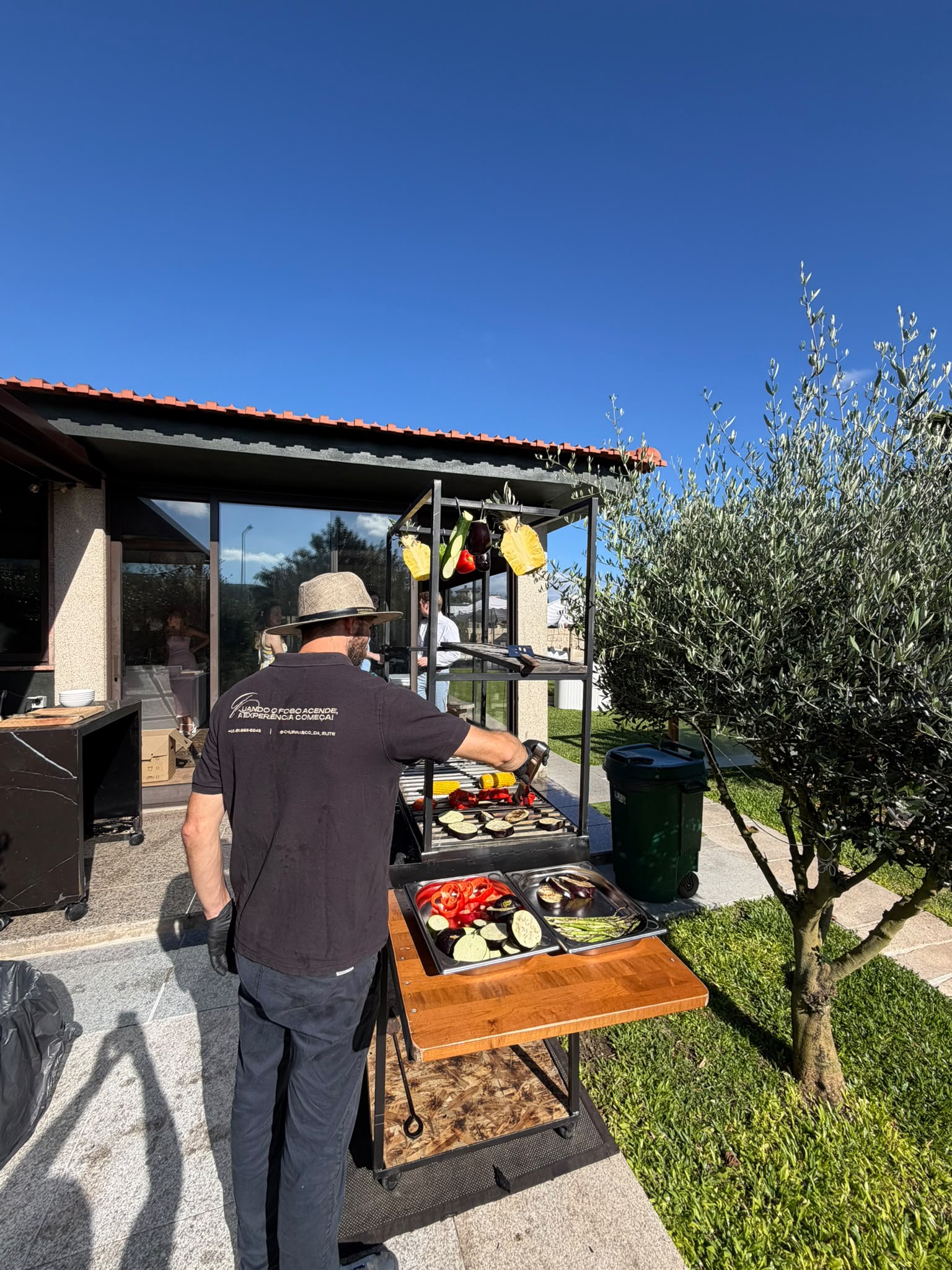 Chef do Churrasco da Elite a grelhar legumes frescos na parrilla num pátio ensolarado