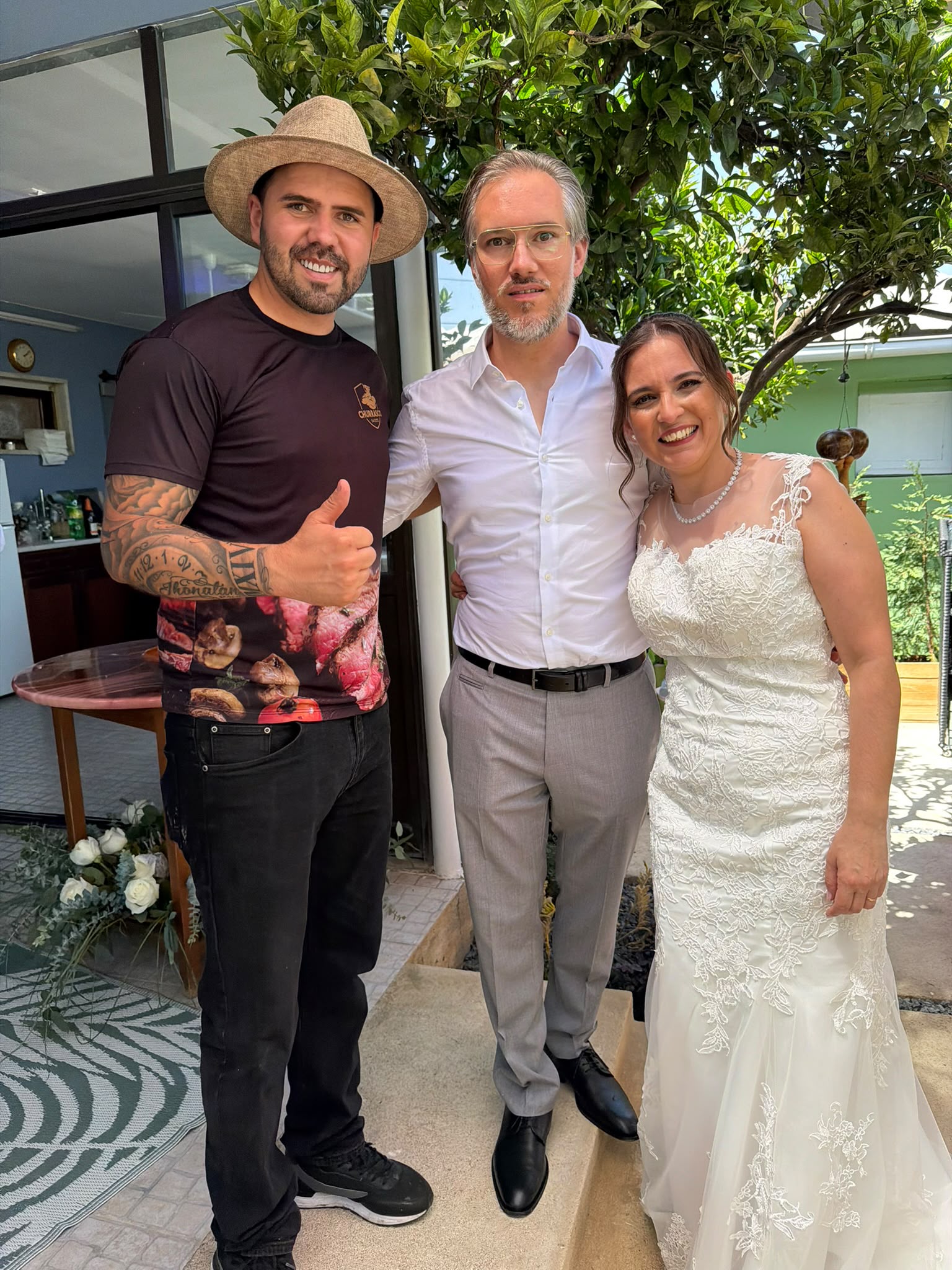 Churrasqueiro sorridente com polegar levantado ao lado dos noivos num casamento ao ar livre