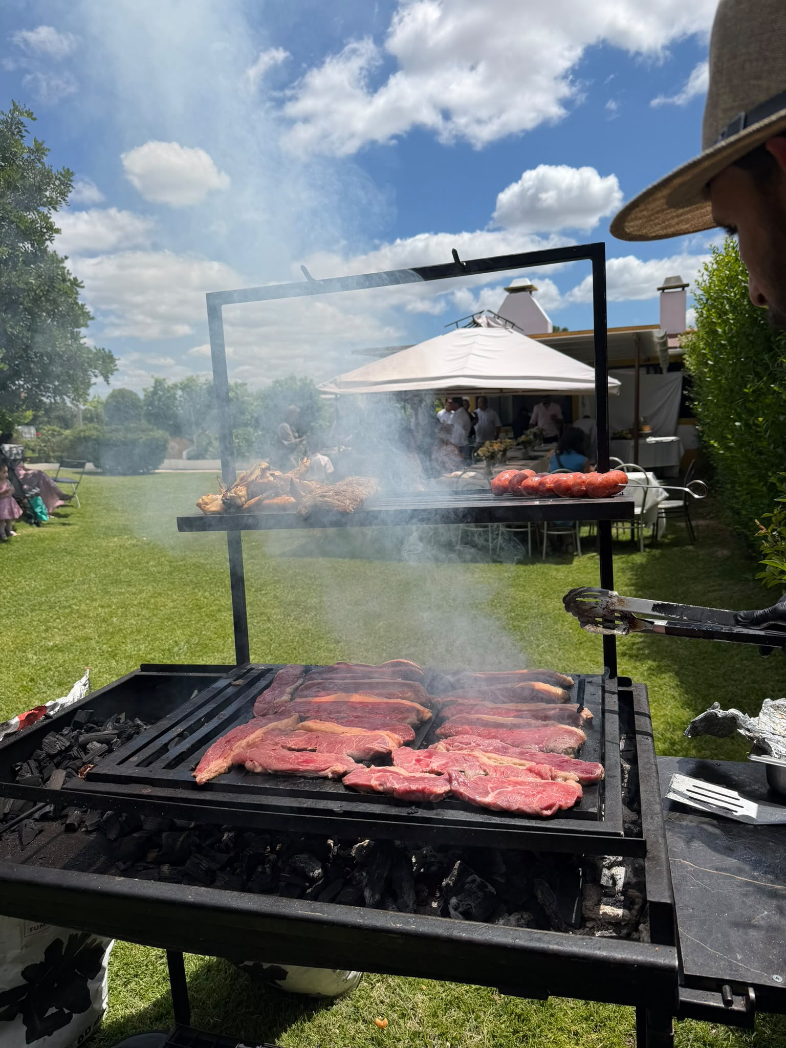 Bifes e salsichas artesanais a grelhar sobre brasas ardentes num evento de catering ao ar livre